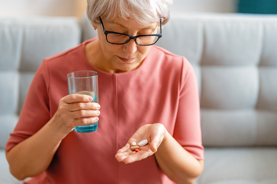 Senior woman holding pills in the palm of her right hand and a glass of water in her left hand