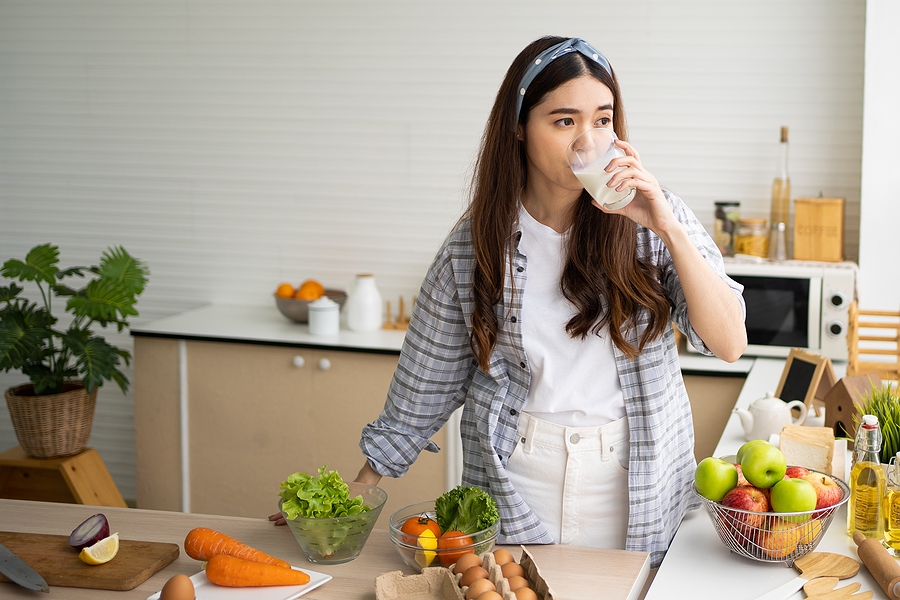Young woman drinking a glass of milk with fruits and vegetables